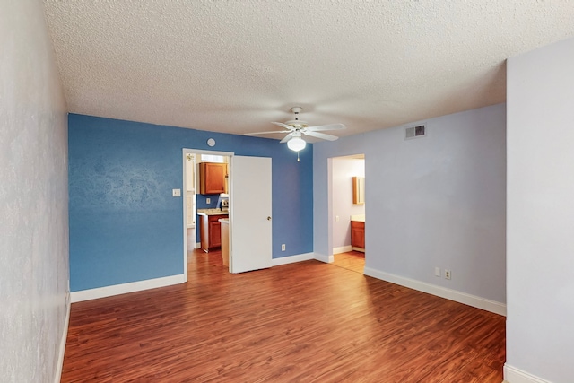 spare room with ceiling fan, a textured ceiling, baseboards, wood finished floors, and visible vents