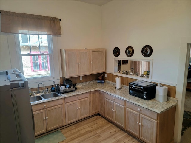 kitchen with a peninsula, refrigerator, light wood-style floors, light stone counters, and a sink