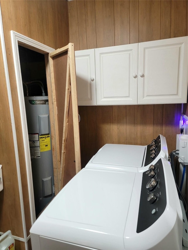 washroom with water heater, cabinet space, wooden walls, and independent washer and dryer