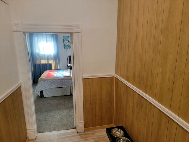 hall with light wood-type flooring, wainscoting, wood walls, and light carpet