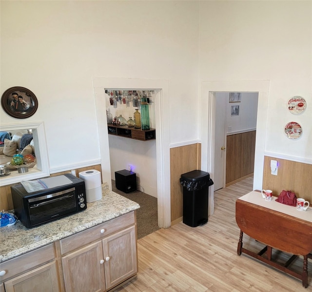 interior space featuring light wood-style flooring, a wainscoted wall, light stone countertops, and a toaster