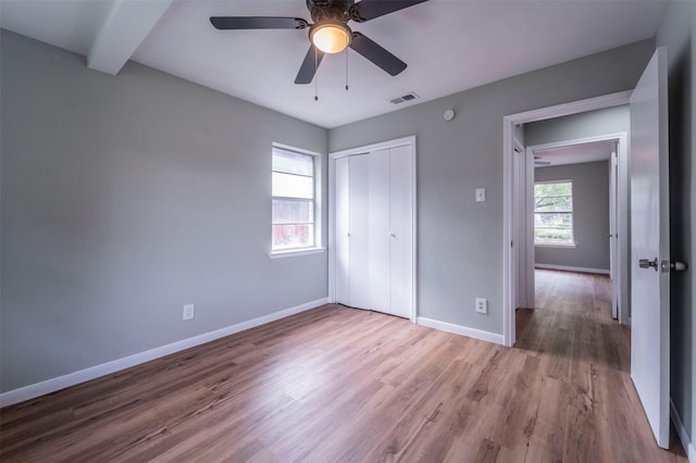 unfurnished bedroom with visible vents, a closet, wood finished floors, baseboards, and ceiling fan