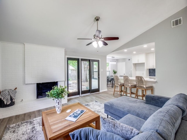 living area with light wood-type flooring, ceiling fan, vaulted ceiling, and a fireplace