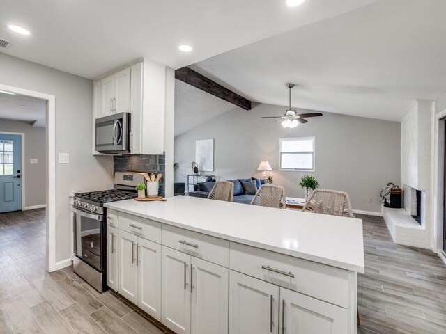 kitchen with white cabinets, light wood finished floors, stainless steel appliances, open floor plan, and a peninsula