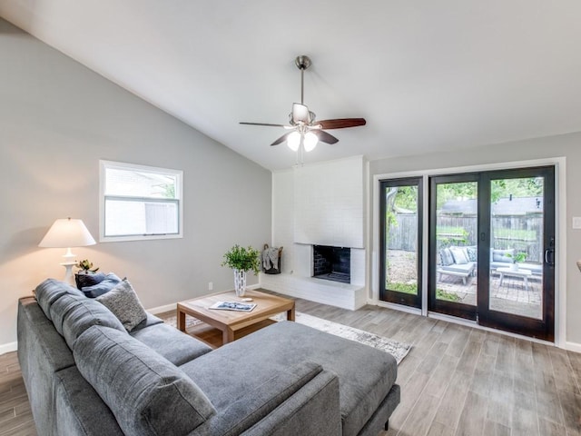 living room featuring a fireplace, baseboards, ceiling fan, light wood-type flooring, and vaulted ceiling