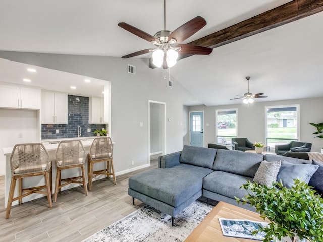 living area featuring ceiling fan, visible vents, light wood-type flooring, baseboards, and lofted ceiling with beams