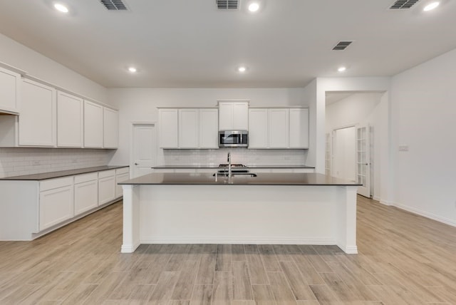 kitchen with a kitchen island with sink, visible vents, dark countertops, tasteful backsplash, and stainless steel microwave