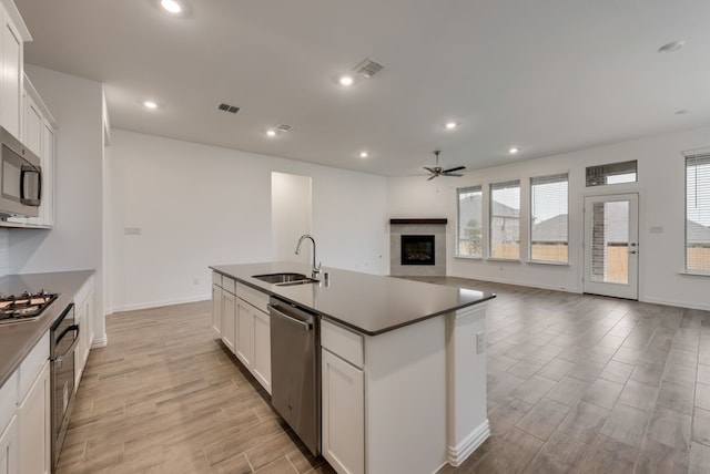 kitchen with ceiling fan, visible vents, a sink, a glass covered fireplace, and stainless steel appliances
