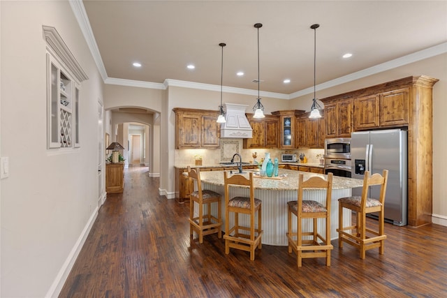 5916 River Highlands Dr, Mckinney, TX 75070 - kitchen featuring stainless steel appliances, premium range hood, brown cabinets, arched walkways, and dark wood-style floors