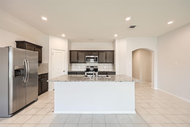 kitchen featuring appliances with stainless steel finishes, tasteful backsplash, light stone countertops, and arched walkways