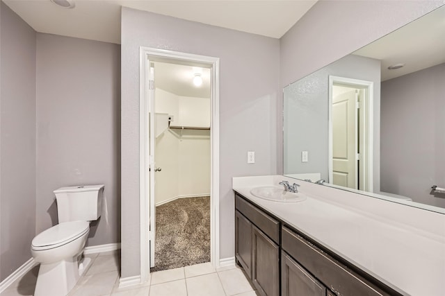 bathroom featuring a walk in closet, tile patterned flooring, vanity, baseboards, and toilet