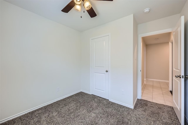 unfurnished bedroom with light tile patterned floors, baseboards, ceiling fan, and light carpet