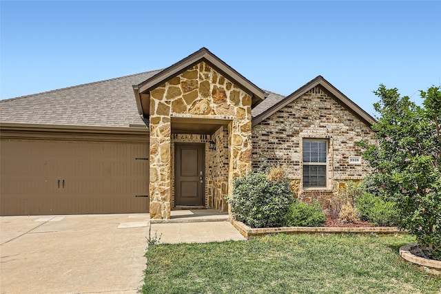 view of front of home featuring driveway, roof with shingles, a front yard, a garage, and stone siding