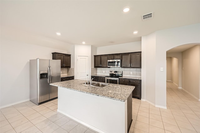 kitchen with dark brown cabinets, appliances with stainless steel finishes, a sink, arched walkways, and tasteful backsplash
