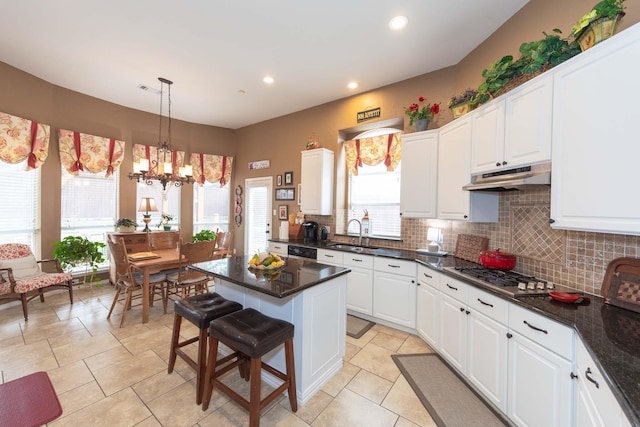kitchen featuring white cabinets, a sink, stainless steel gas cooktop, backsplash, and under cabinet range hood