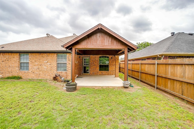 rear view of house featuring fence, a patio, brick siding, a shingled roof, and a yard