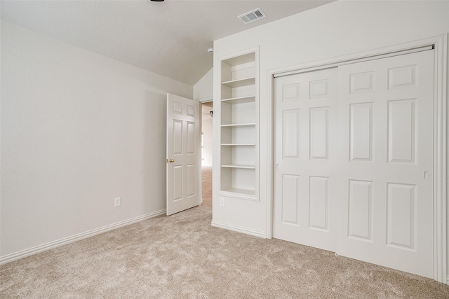 unfurnished bedroom featuring visible vents, a closet, lofted ceiling, light carpet, and baseboards