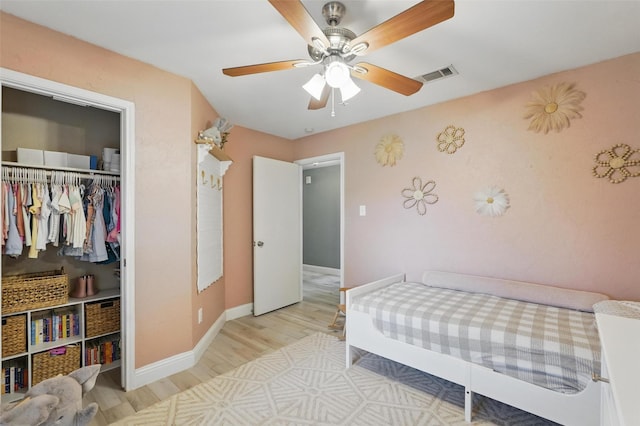 bedroom with a ceiling fan, baseboards, wood finished floors, visible vents, and a closet