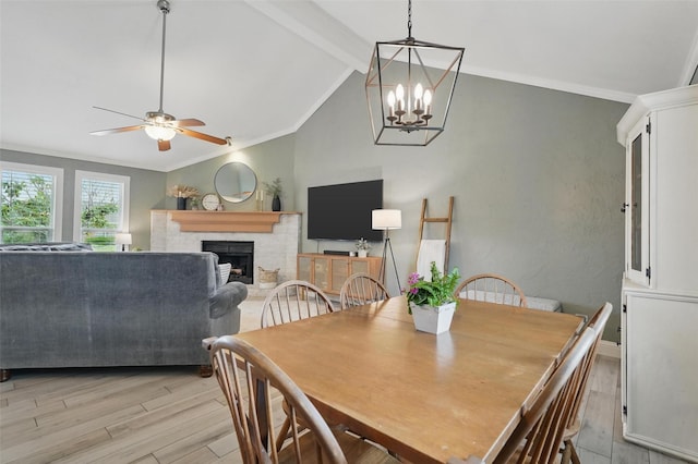 dining area featuring vaulted ceiling with beams, a fireplace, ceiling fan with notable chandelier, and light wood-style flooring