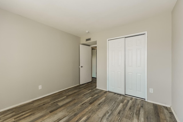 unfurnished bedroom with baseboards, a closet, dark wood-style floors, and visible vents