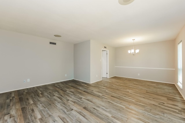 unfurnished room featuring wood finished floors, baseboards, a chandelier, and visible vents