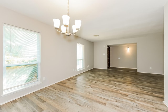 unfurnished room featuring baseboards, wood finished floors, and a notable chandelier