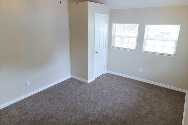 unfurnished room with baseboards and dark colored carpet