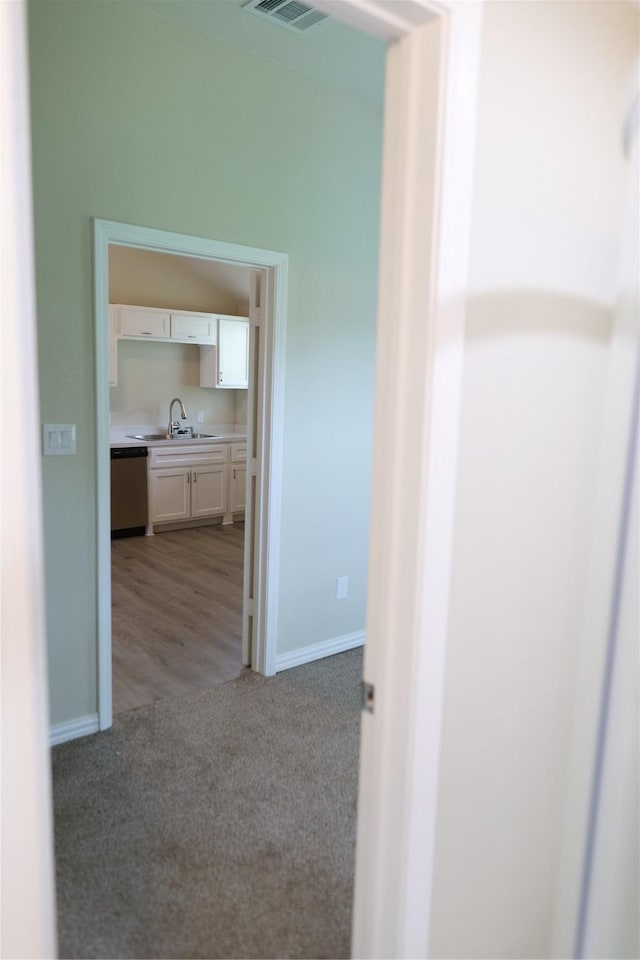 hall featuring a sink, baseboards, light carpet, and visible vents