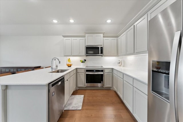 kitchen featuring decorative backsplash, a peninsula, light wood-type flooring, a sink, and appliances with stainless steel finishes