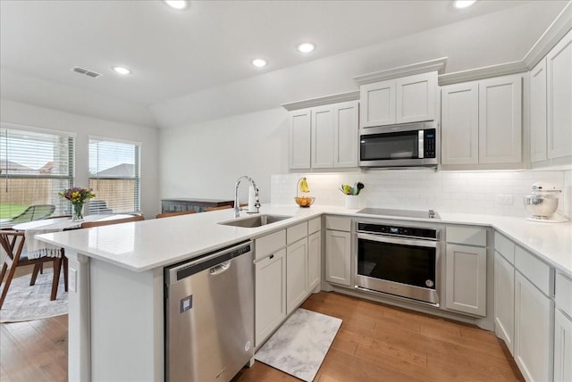 kitchen featuring visible vents, a peninsula, light countertops, a sink, and appliances with stainless steel finishes