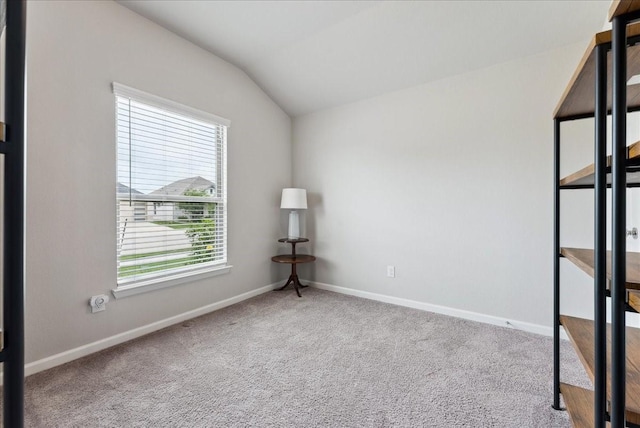 carpeted spare room featuring baseboards, vaulted ceiling, and a wealth of natural light