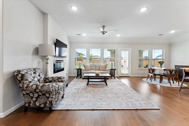 living room with a ceiling fan, visible vents, baseboards, a glass covered fireplace, and hardwood / wood-style floors