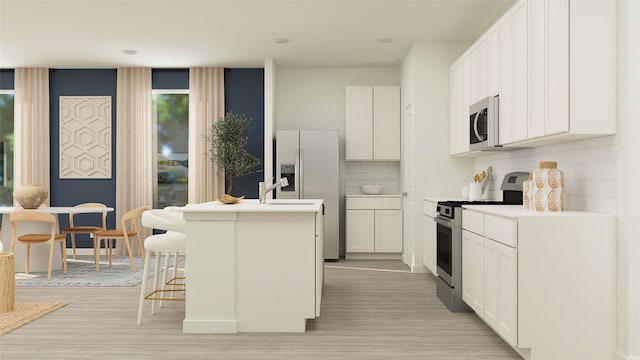 kitchen with a kitchen breakfast bar, backsplash, appliances with stainless steel finishes, a center island with sink, and light wood finished floors
