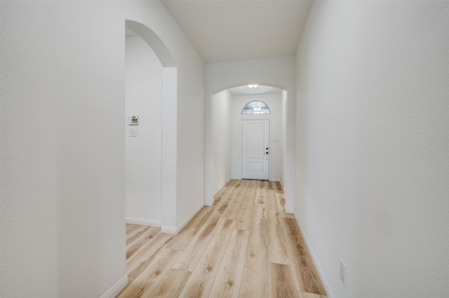 hall featuring light wood-type flooring, arched walkways, and baseboards