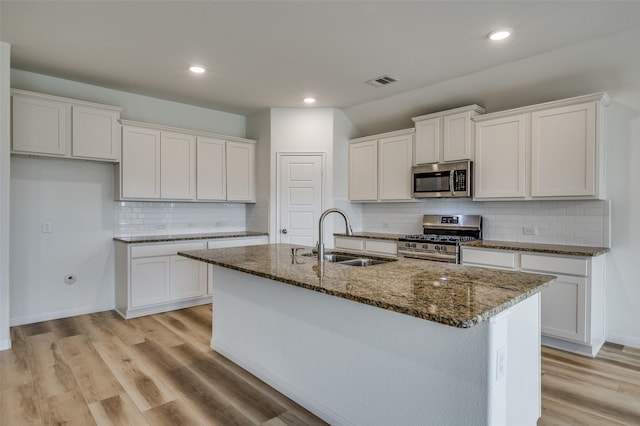 kitchen with a sink, dark stone counters, stainless steel appliances, and visible vents