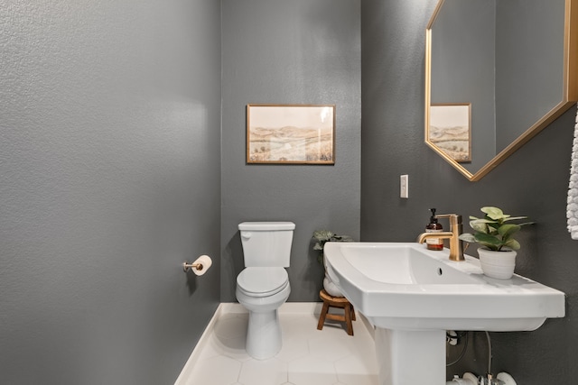 bathroom featuring baseboards, a textured wall, tile patterned floors, and toilet
