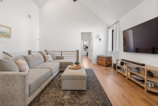 living area featuring wood-type flooring, high vaulted ceiling, visible vents, and baseboards