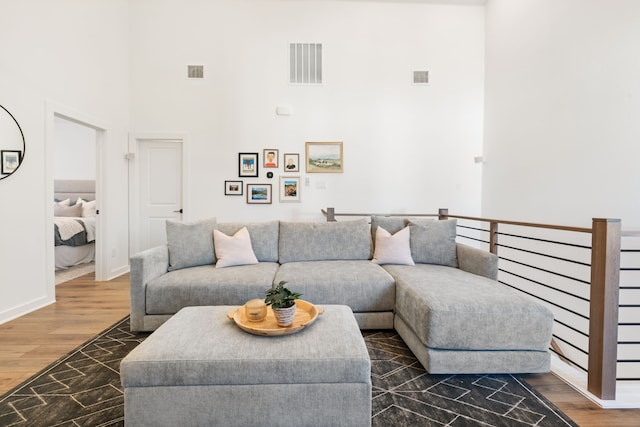 living room featuring baseboards, a high ceiling, visible vents, and wood finished floors