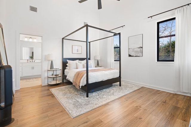 bedroom with a towering ceiling, multiple windows, light wood finished floors, and visible vents
