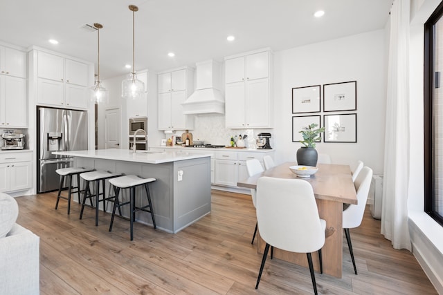 kitchen featuring a kitchen breakfast bar, backsplash, a sink, custom exhaust hood, and stainless steel appliances