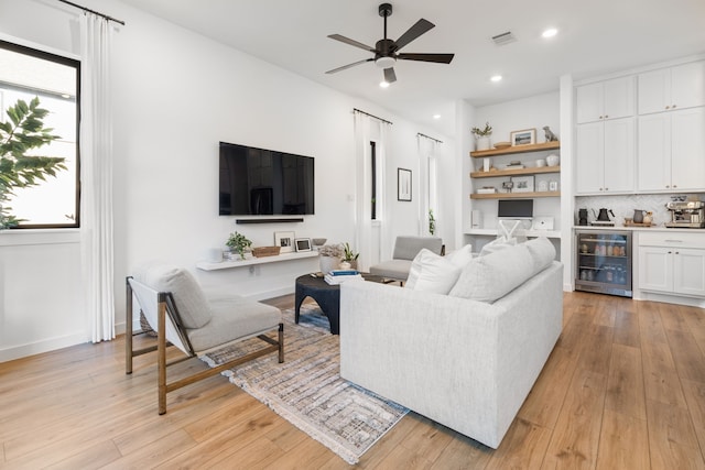 living area with visible vents, a ceiling fan, wine cooler, and light wood-type flooring