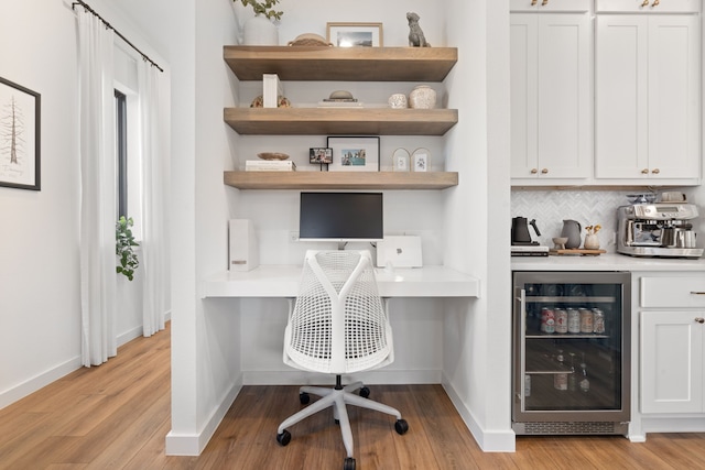office area with beverage cooler, baseboards, built in desk, and light wood finished floors