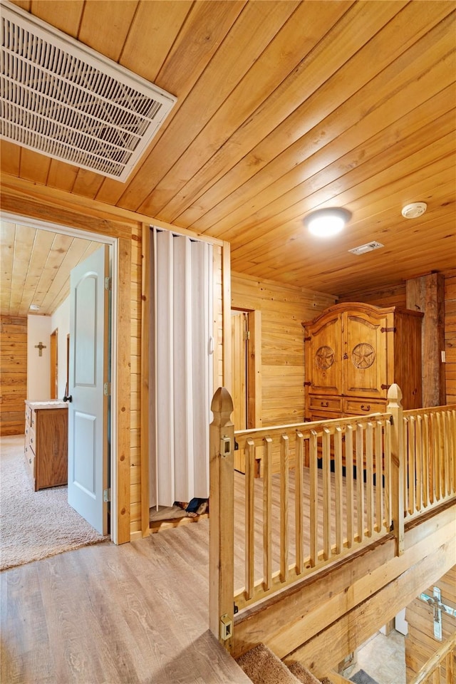 corridor with wood walls, an upstairs landing, wooden ceiling, and visible vents
