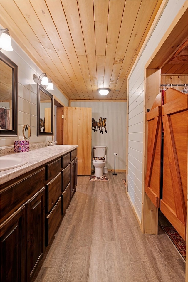 full bath with double vanity, wood finished floors, toilet, wooden ceiling, and a sink