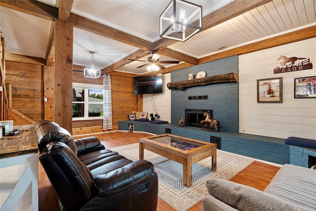 living room featuring wood walls, a brick fireplace, wood finished floors, and beamed ceiling