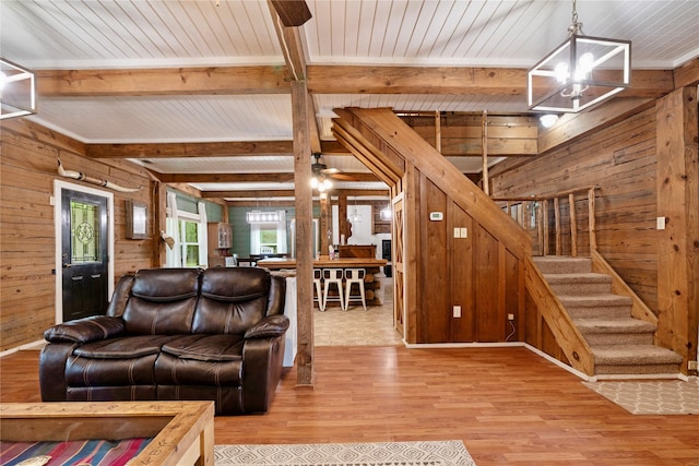 living area with wooden walls, a notable chandelier, stairs, wood finished floors, and beamed ceiling