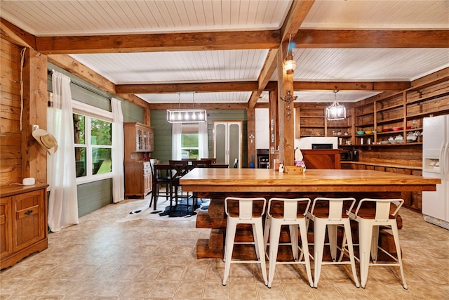kitchen with wood walls, pendant lighting, beamed ceiling, butcher block countertops, and white fridge with ice dispenser