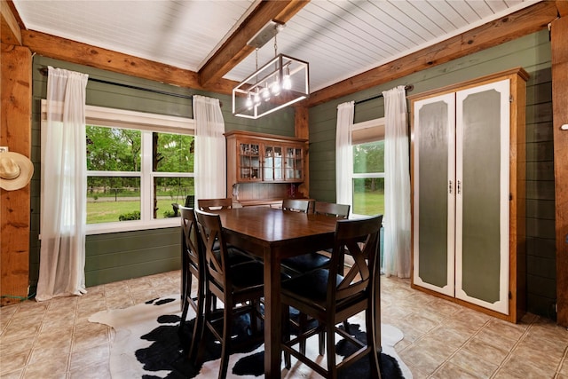 dining room featuring beamed ceiling, wood walls, and a chandelier
