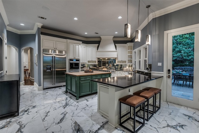 kitchen featuring arched walkways, custom range hood, green cabinetry, stainless steel appliances, and butcher block countertops
