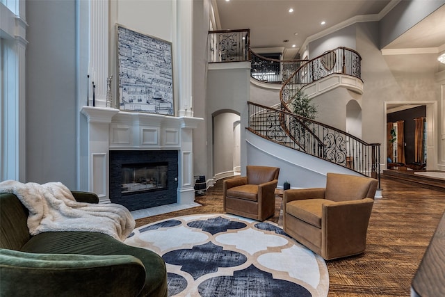 living room featuring a towering ceiling, crown molding, a fireplace with flush hearth, stairway, and recessed lighting